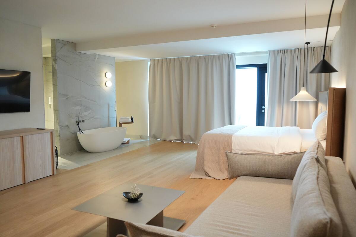 Una habitación de hotel moderna con una cama grande, una zona de estar, una bañera y un televisor.