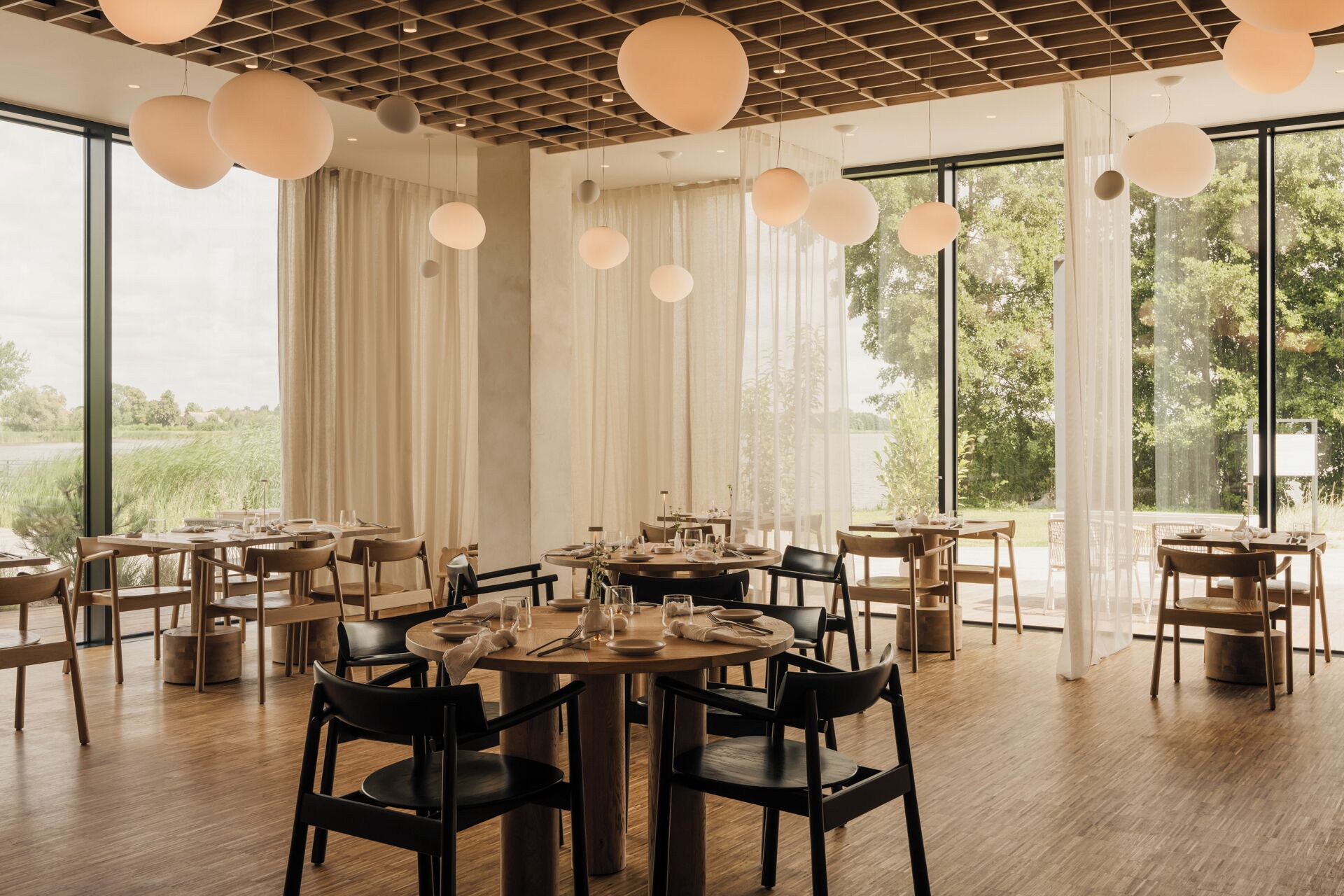 Un restaurante con mesas redondas, sillas negras y lámparas esféricas colgantes.
