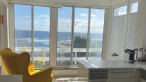 Uma cozinha moderna com vista para o oceano, uma área de jantar com cadeiras amarelas e uma janela grande.
