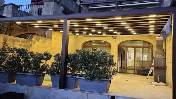 An outdoor patio area with stone walls, potted plants, and a modern lighting system. - Aurelia Gozo BnB (Xaghra)