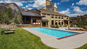 A modern hotel with a large pool, outdoor seating, and a mountainous backdrop.