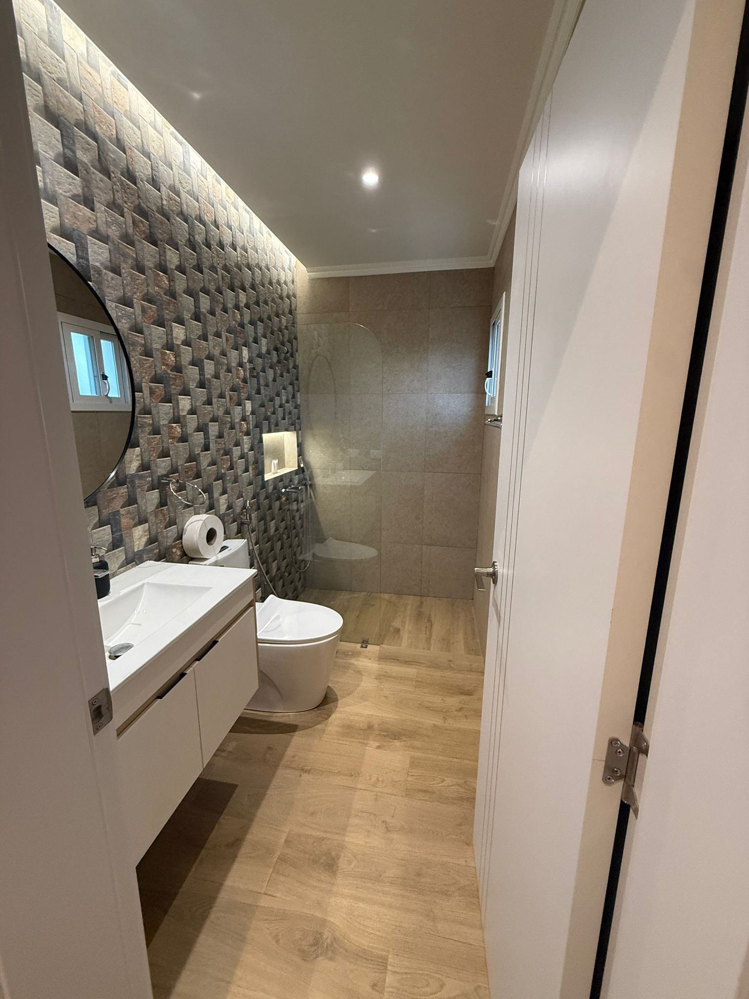 A modern bathroom with a stone wall, a toilet, a sink, and a shower.