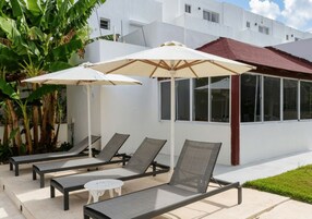 A poolside area with lounge chairs and umbrellas, a white building with large windows, and a red roof.