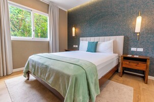 A bedroom with a bed, a nightstand, a window with curtains, and a wall-mounted light fixture.