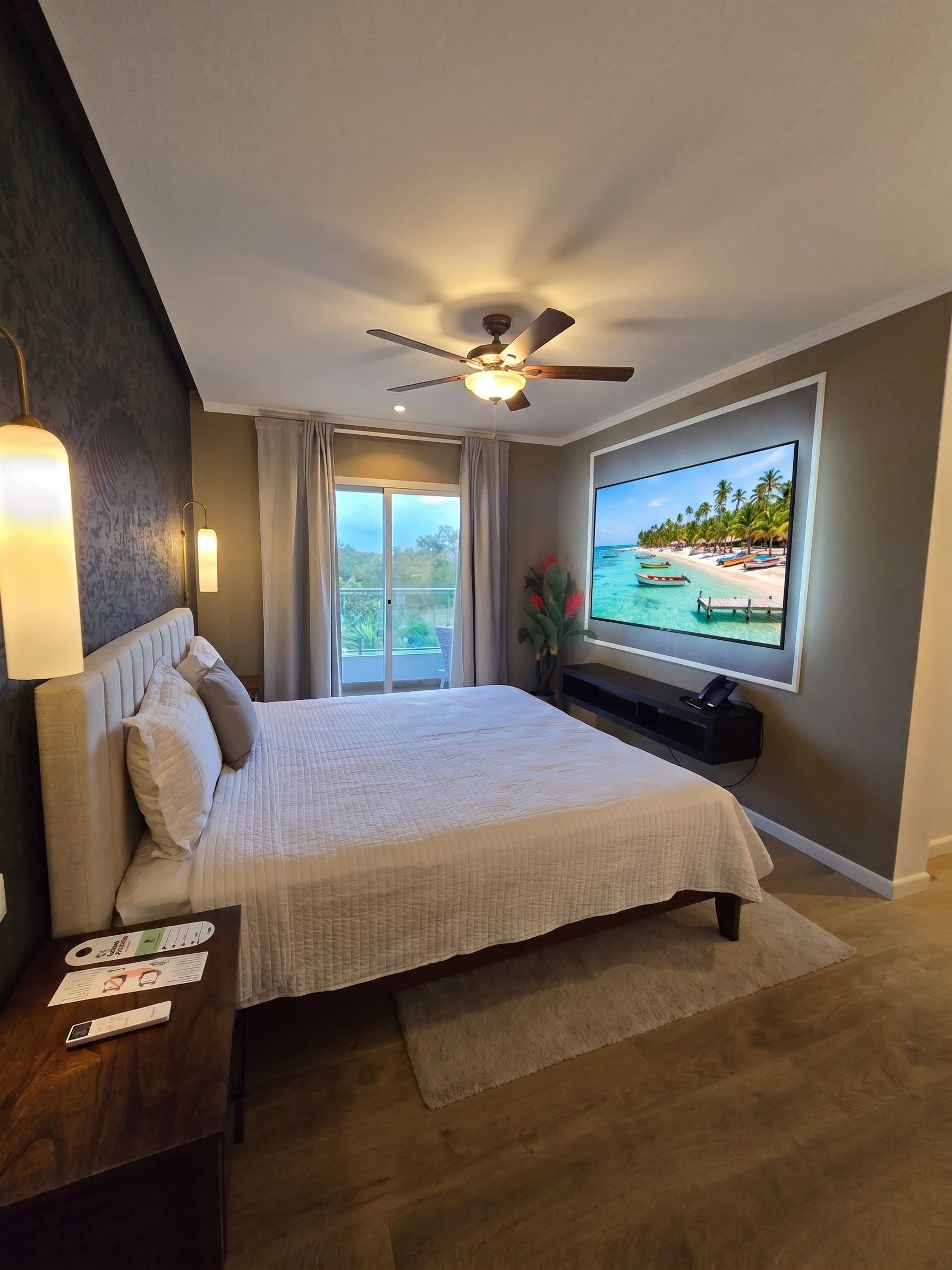 Un dormitorio con cama, ventilador de techo, televisor y vista a la playa.