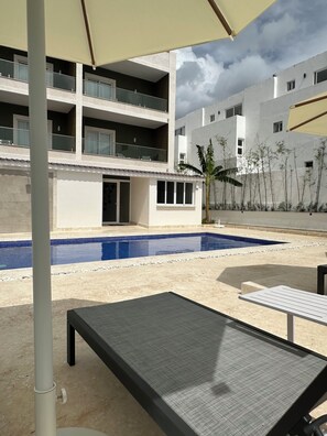 A pool area with lounge chairs, a building with multiple balconies, and a clear sky.