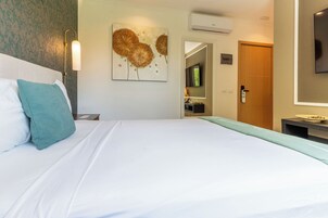 Quarto de hotel com cama, mesa de cabeceira, televisão na parede e porta.