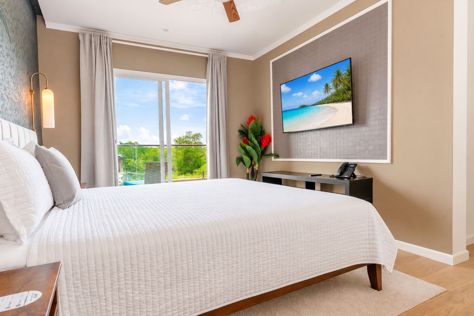 Ein Hotelzimmer mit einem großen Bett, einem an der Wand montierten Flachbildfernseher, einem Schreibtisch mit Telefon und Blick ins Grüne durch das Fenster.