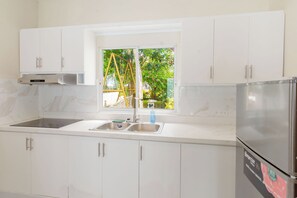 A kitchen with white cabinets, a stainless steel refrigerator, and a window with a view of greenery.