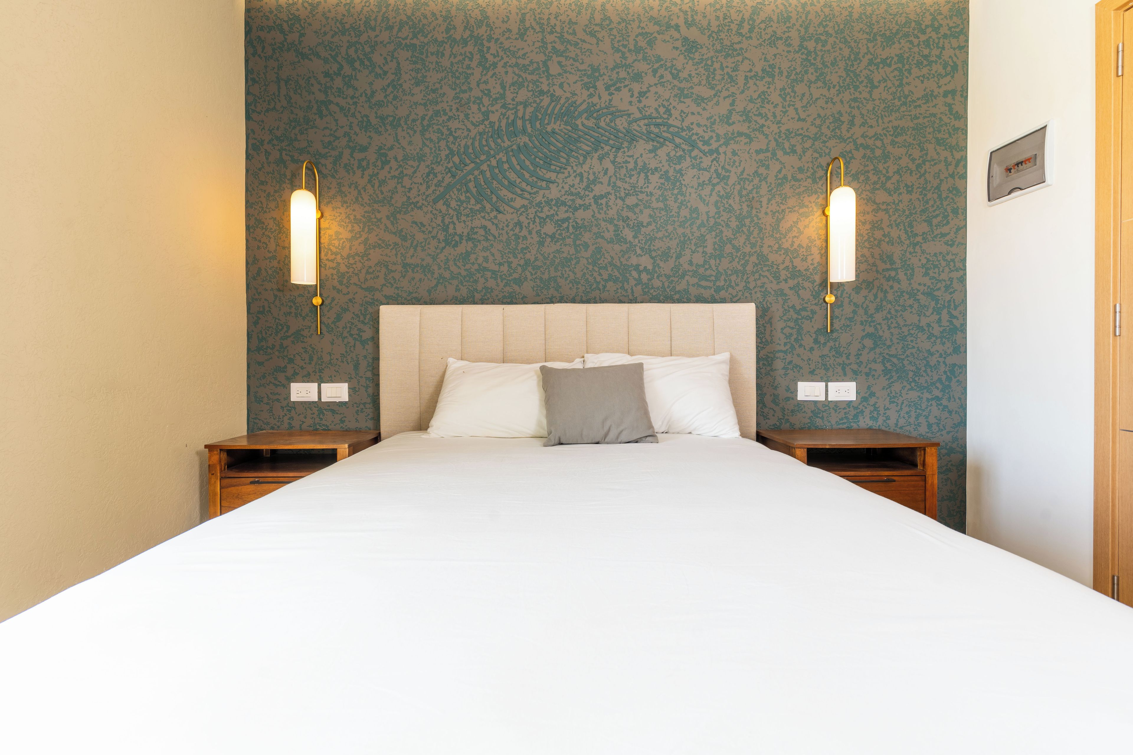 A hotel room with a large bed, two bedside tables, a wooden nightstand, and a wall with a floral pattern.