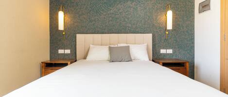 A hotel room with a large bed, two bedside tables, a wooden nightstand, and a wall with a floral pattern.