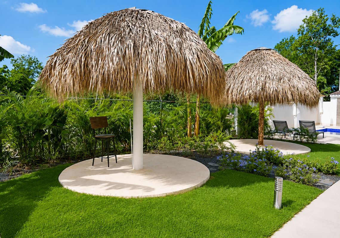 Un jardín tropical con sombrillas de paja, un espacio de estar circular y abundante follaje.