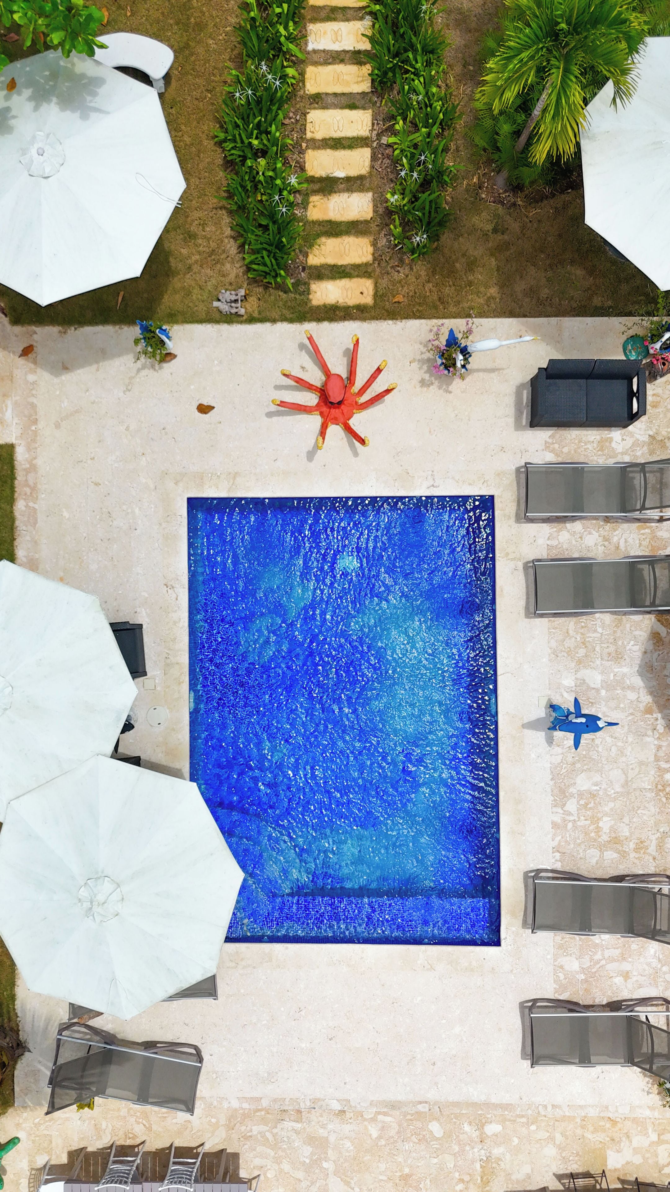 An aerial view of a swimming pool area with a red decorative object, lounge chairs, and umbrellas.