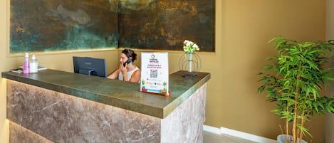 Un comptoir d’accueil d’hôtel avec un plateau en marbre, un panneau indiquant que le Wi-Fi est gratuit et une plante en pot.