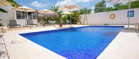 A swimming pool with a tiled edge, surrounded by lounge chairs and umbrellas.