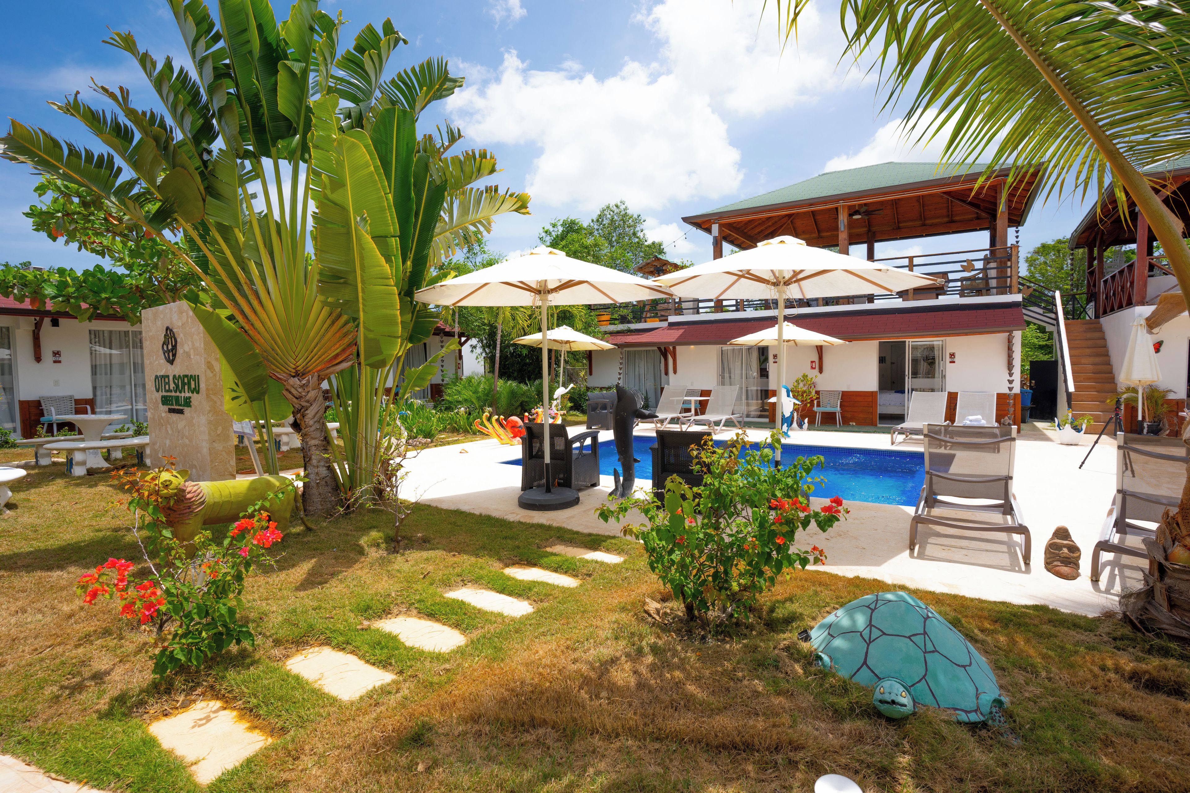A pool area with umbrellas, lounge chairs, and a building with a red roof.