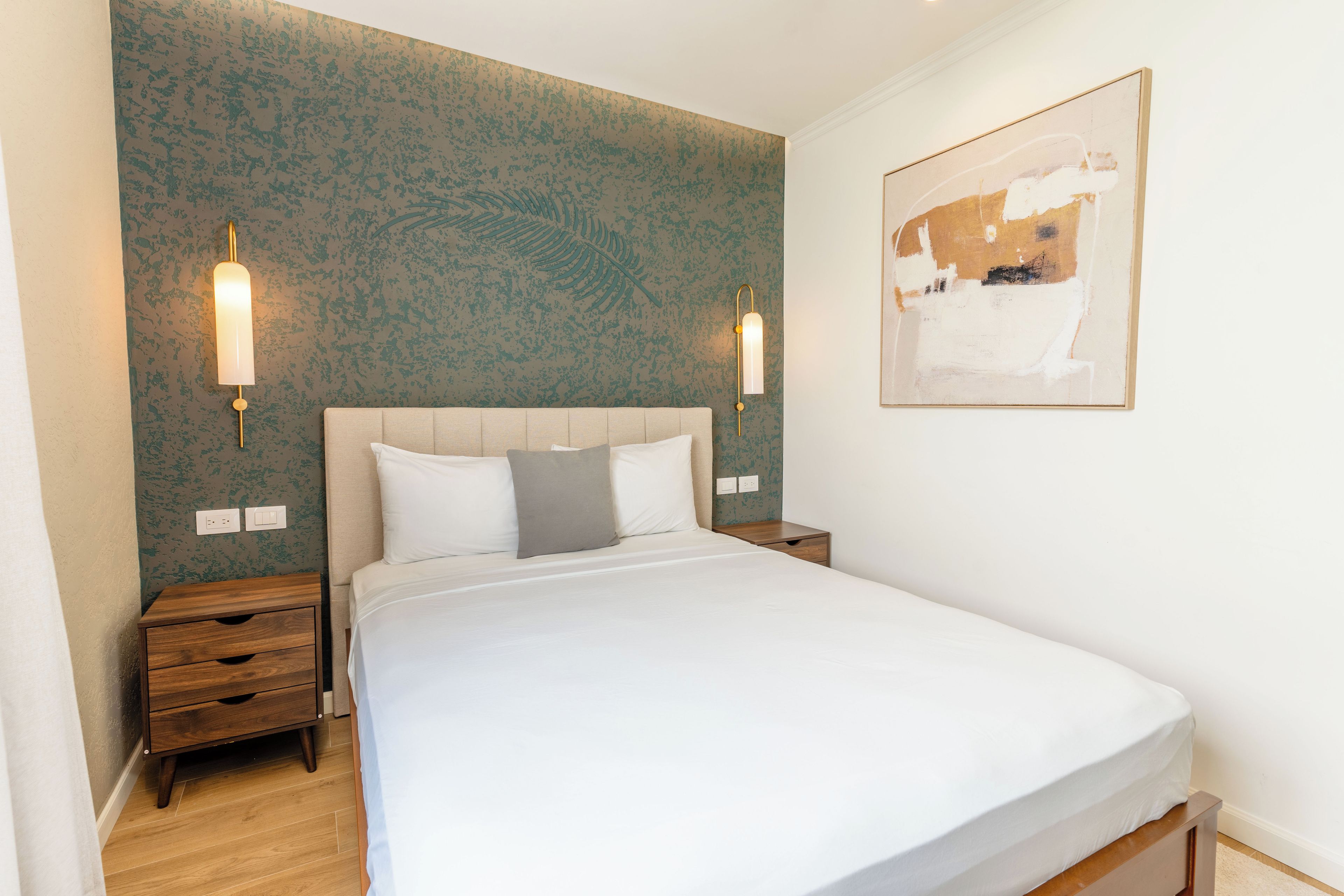 A hotel room with a bed, nightstands, a wall-mounted light fixture, and a painting.