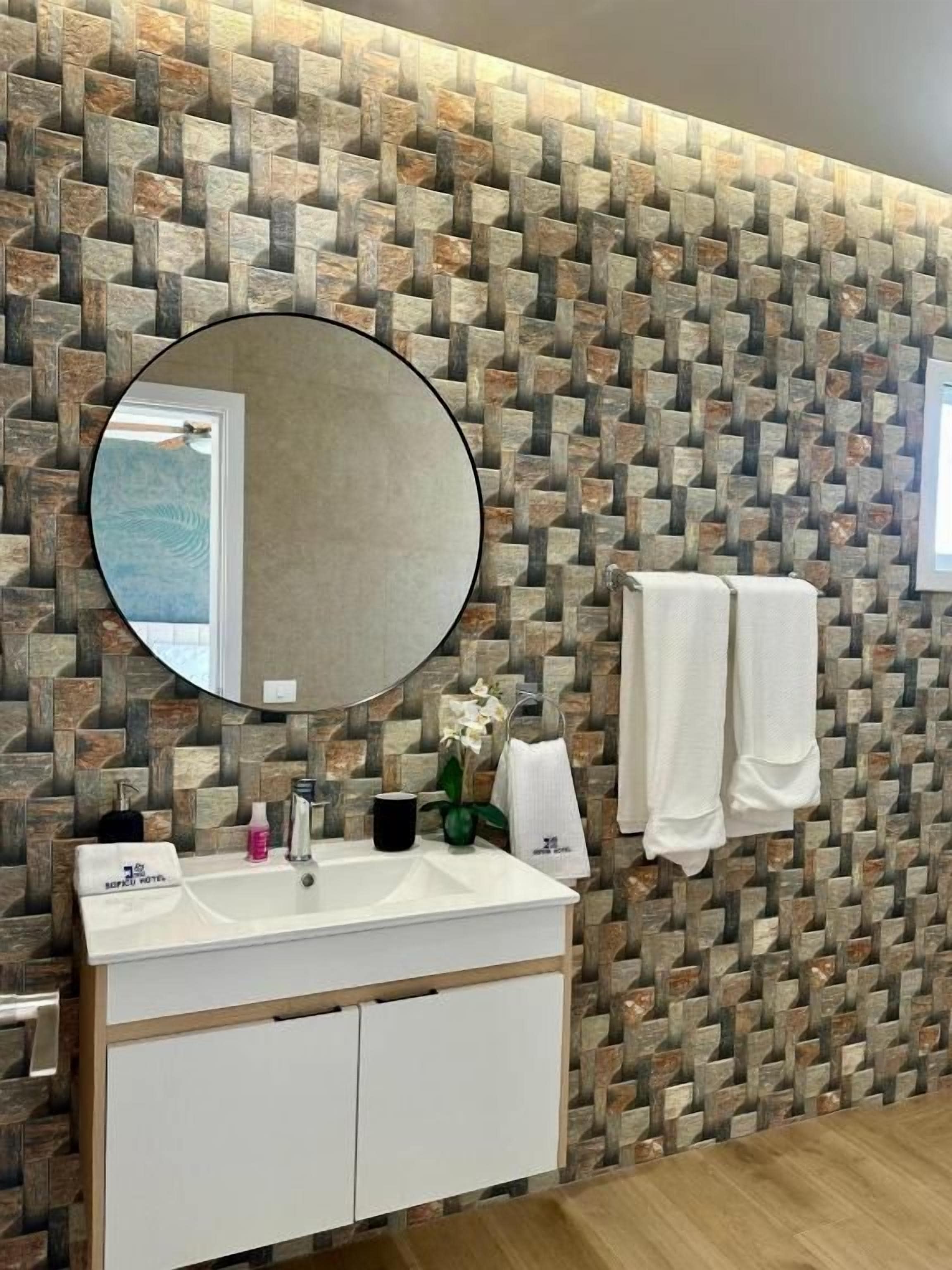 A bathroom with a stone-patterned wall, a round mirror, a white sink, and two towels.