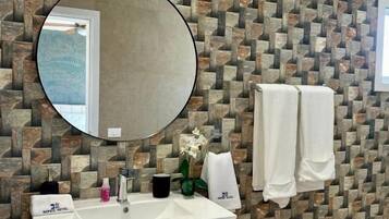 A bathroom with a stone-patterned wall, a round mirror, a white sink, and two towels.