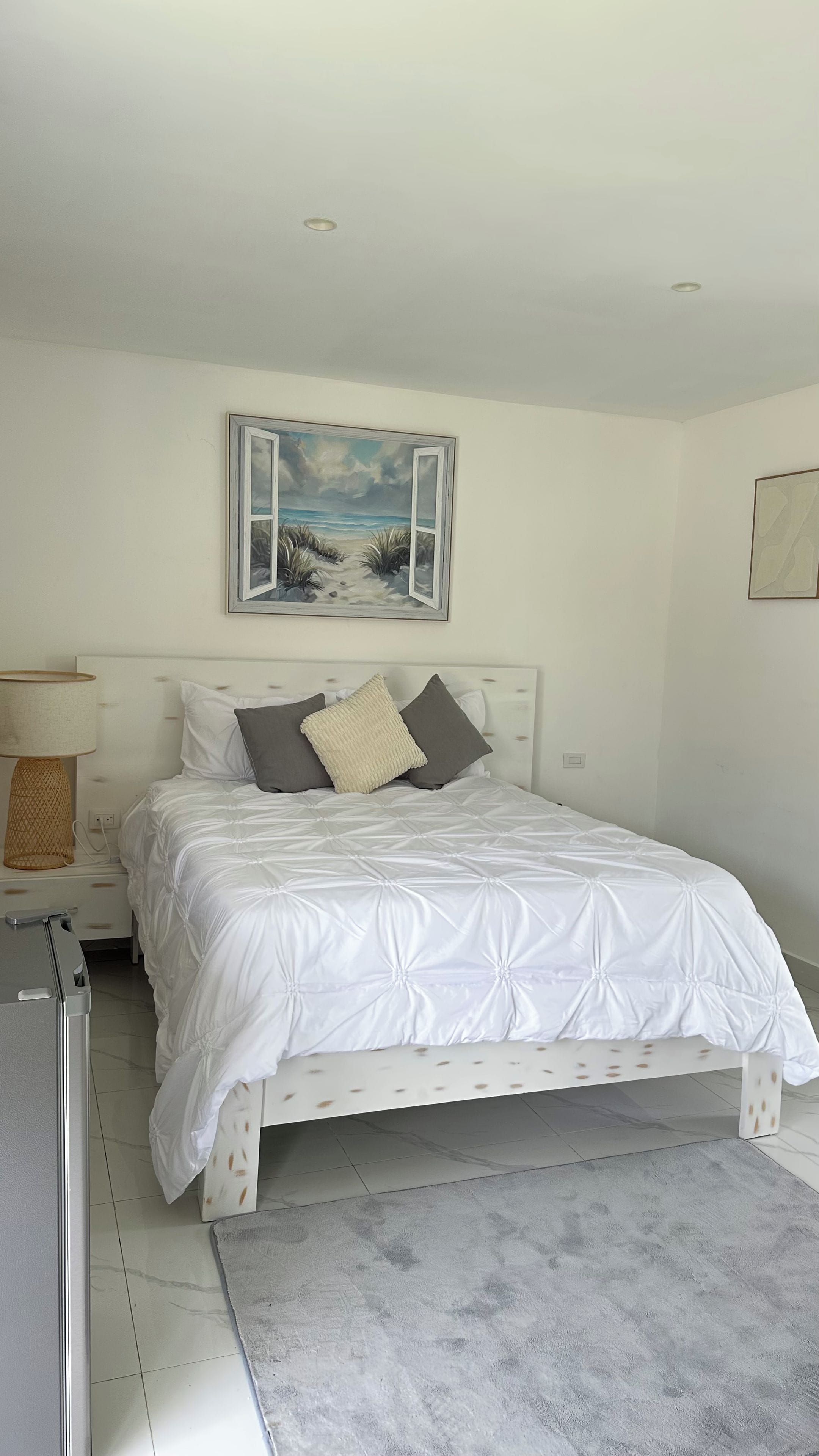 A bedroom with a bed, a nightstand, a lamp, a painting, and a rug.