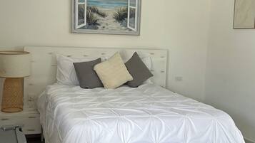 A bedroom with a bed, a nightstand, a lamp, a painting, and a rug.