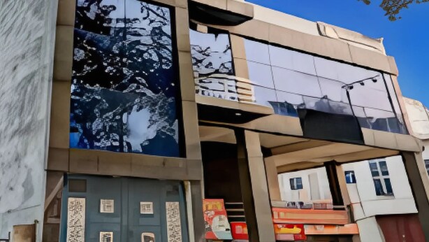 A modern building with a glass facade, a prominent logo on the upper level, and a series of windows. - Hotel Shimla Grand (Lucknow)
