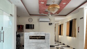 A reception area with a marble counter, a clock, a television, and a ceiling fan. - Hotel Shimla Grand (Lucknow)