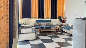 A modern living room with a checkered floor, a sofa set, a coffee table, and a ceiling fan. - Hotel Shimla Grand (Lucknow)