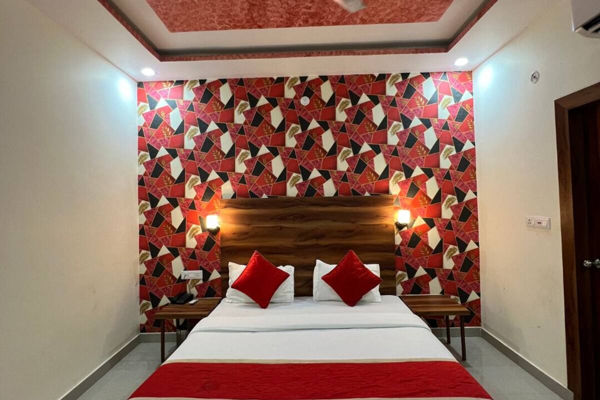 A hotel room with a bed, a ceiling fan, a patterned wall, and a wooden headboard.