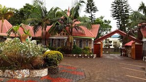 A hotel with a red-roofed building, surrounded by tropical vegetation and palm trees. - Nuru Palace Hotel (Nakuru)