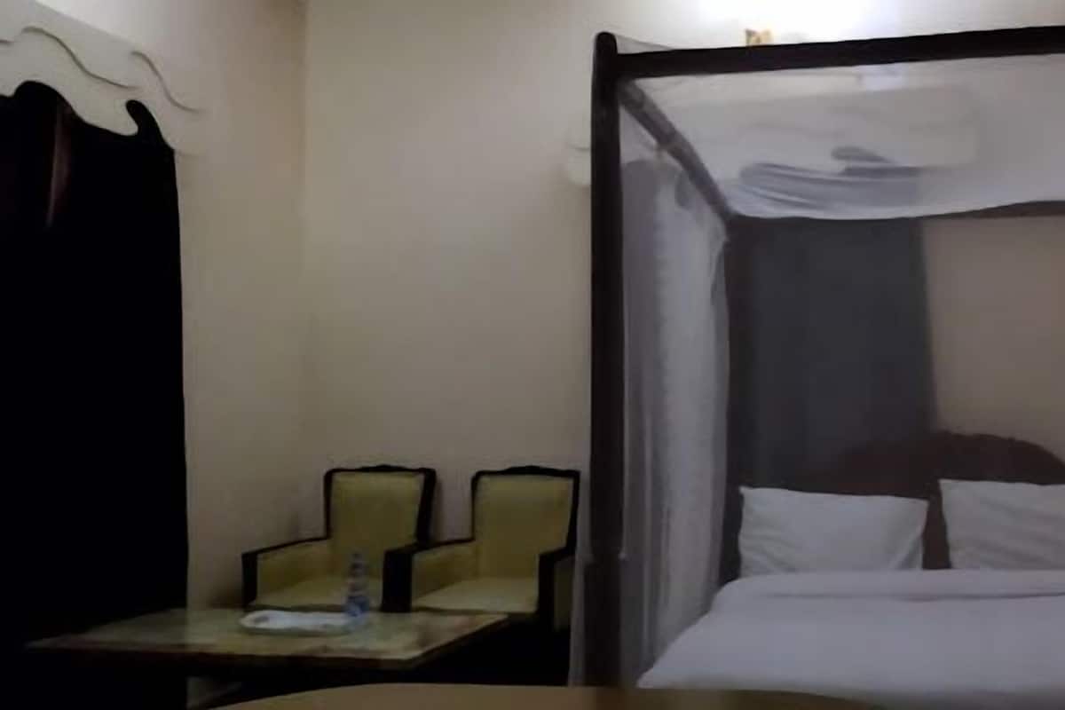 Una cama individual con dosel, una mesita con una silla y una cortina.