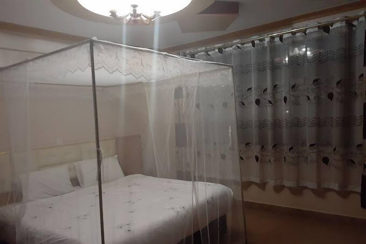 Una cama con dosel, una cortina con estampado y un candelabro.