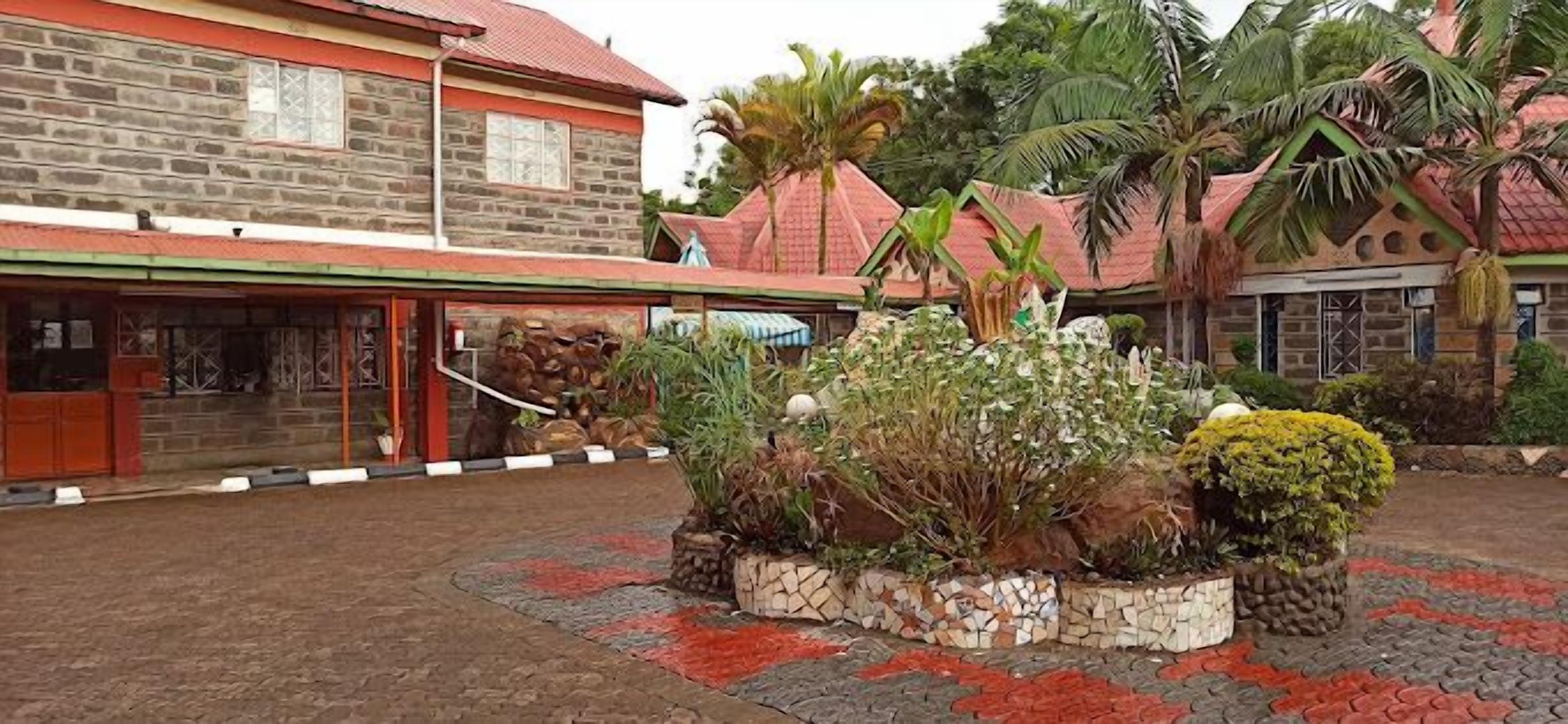 Un bâtiment en pierre avec un toit rouge et une cour pavée agrémentée de plantes et d’une bordure décorative.