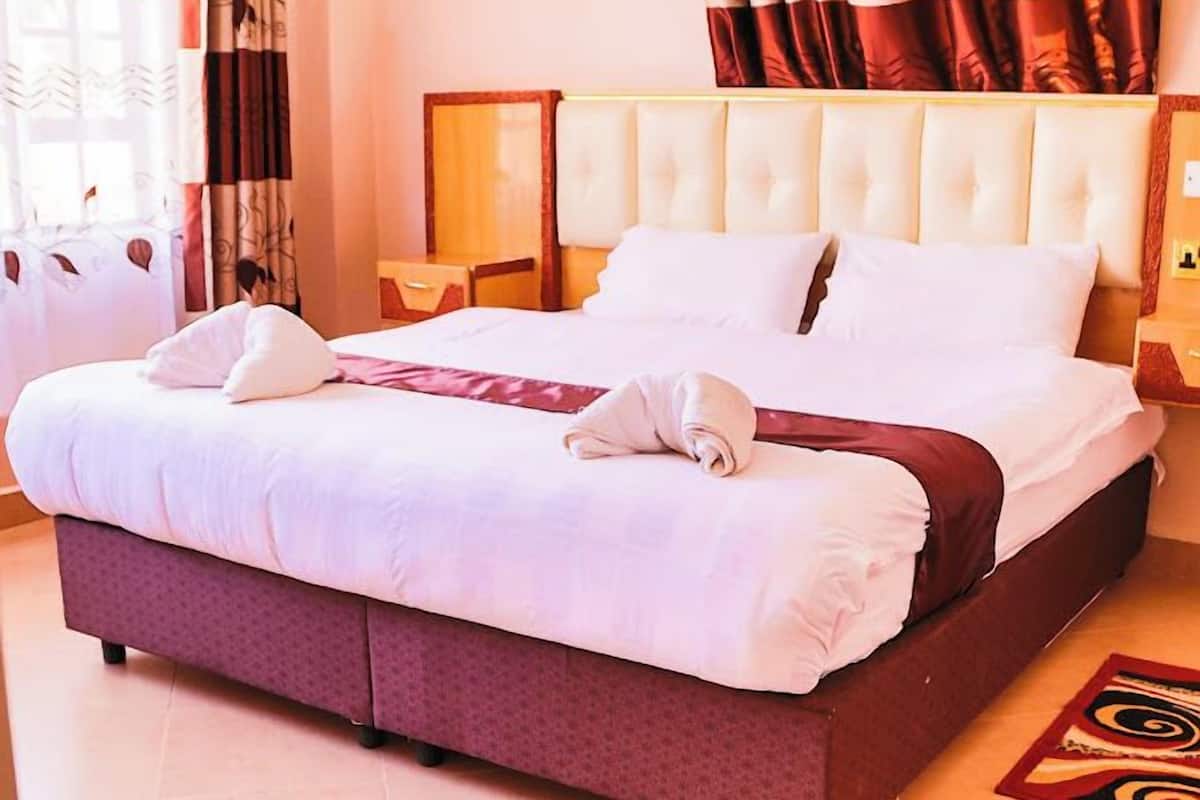 Habitación de hotel con una cama grande, cabecera, mesita de noche y ventana con cortinas.