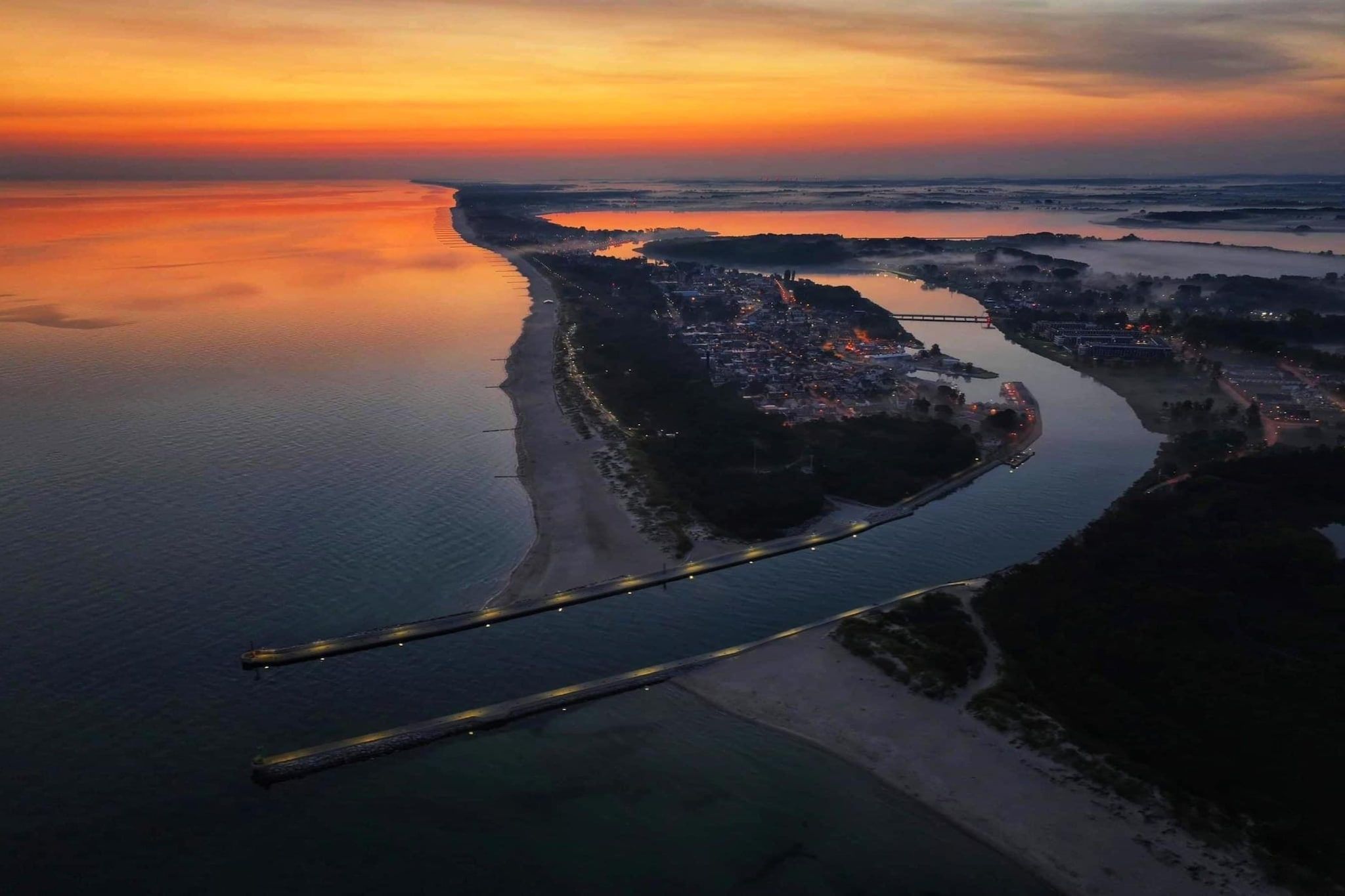 An aerial view of a coastal city at sunset with a prominent bridge and a peninsula.