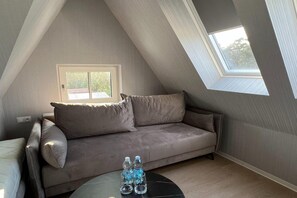 A room with a sloped ceiling, a sofa, a small table with water bottles, and a window.