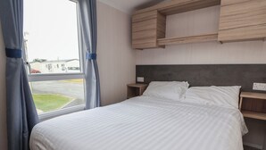 Habitación de hotel con una cama grande, cabecero, mesita de noche y ventana con cortinas.