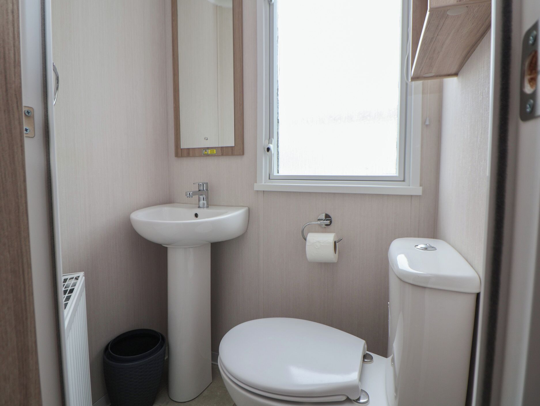 A compact bathroom with a white sink, toilet, and a small window.