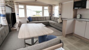 Interior compacto de una caravana con comedor, sofá, kitchenette y televisor.