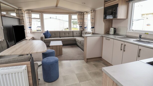 Cocina compacta para vehículos recreativos, con zona de comedor, microondas integrado y ventana con cortinas.