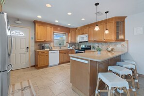 A kitchen with wooden cabinets, a microwave, a dishwasher, and a large island with bar stools.