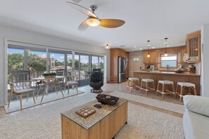 A spacious living area with a large sliding glass door leading to a balcony, a central coffee table, and a kitchen with wooden cabinets and a refrigerator.