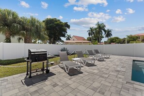 An outdoor patio with a pool, lounge chairs, and a barbecue grill.
