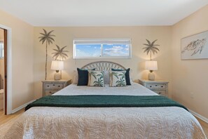 A bedroom with a bed, two nightstands, a window with a view, and a wall with a painting.