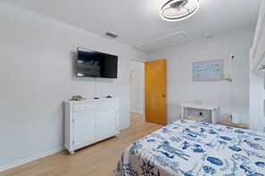 A bedroom with a bed, a TV mounted on a white cabinet, a wooden door, and a small desk with a chair.