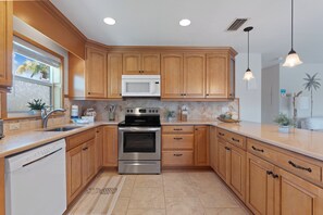 A kitchen with wooden cabinets, a stainless steel oven, a microwave, and a window with a view of palm trees.