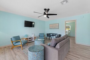 Un salon comprenant un canapé, des fauteuils, une table basse, un téléviseur et un ventilateur de plafond.