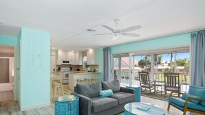 Een moderne woonkamer met een grijze bank, een blauw getextureerde salontafel en een balkon met tuinmeubilair.