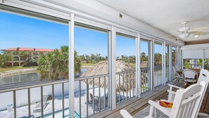 A covered outdoor area with a pool, white chairs, and a view of a building with a red roof. - ☀️Private Pool, Fun Outdoor Area🐾Pet Friendly🐾Vallie's Villa & Monty's Place☀️ (Fort Myers Beach)