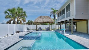 A swimming pool with a thatched roof, lounge chairs, and a view of a building with large windows. - ☀️Private Pool, Fun Outdoor Area🐾Pet Friendly🐾Vallie's Villa & Monty's Place☀️ (Fort Myers Beach)